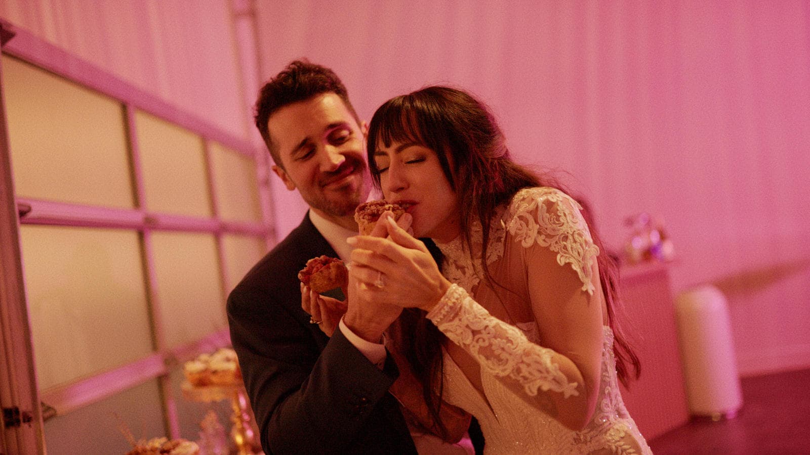 wedding couple eating cake in glow of neon pink light